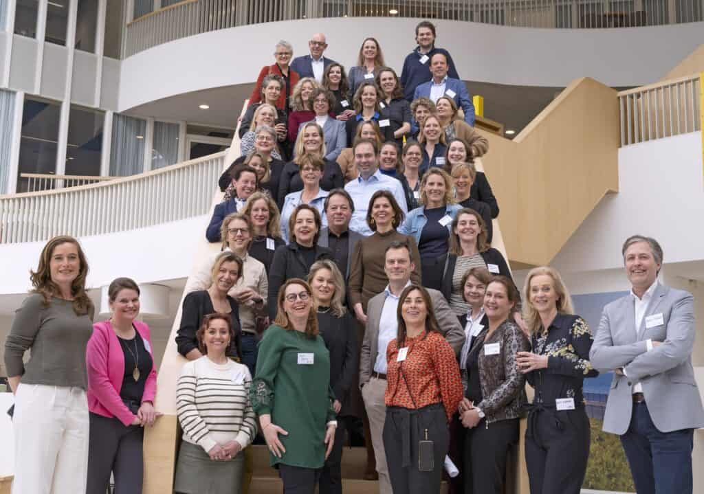 Een groep van ongeveer 50 mensen staat op een trap. Ze kijken allemaal in de camera.
